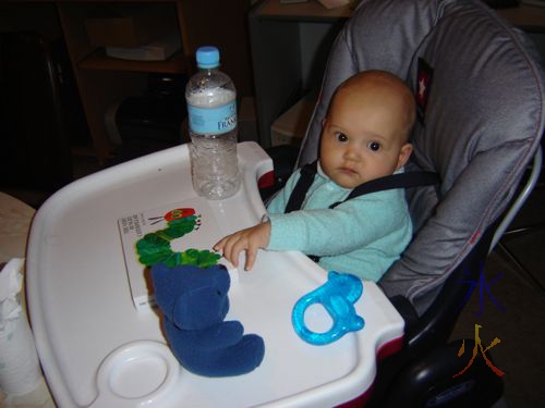 baby in highchair with book and toys