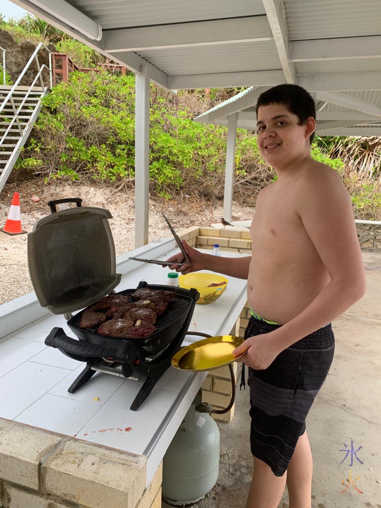 15yo cooking steak on a small barbeque thing at Lily Beach, Christmas Island