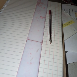A4 notebook being ruled up with red lines by a red ball point pen