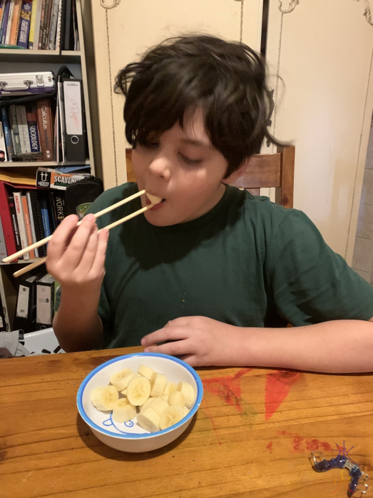 11yo eating banana slices with chopsticks
